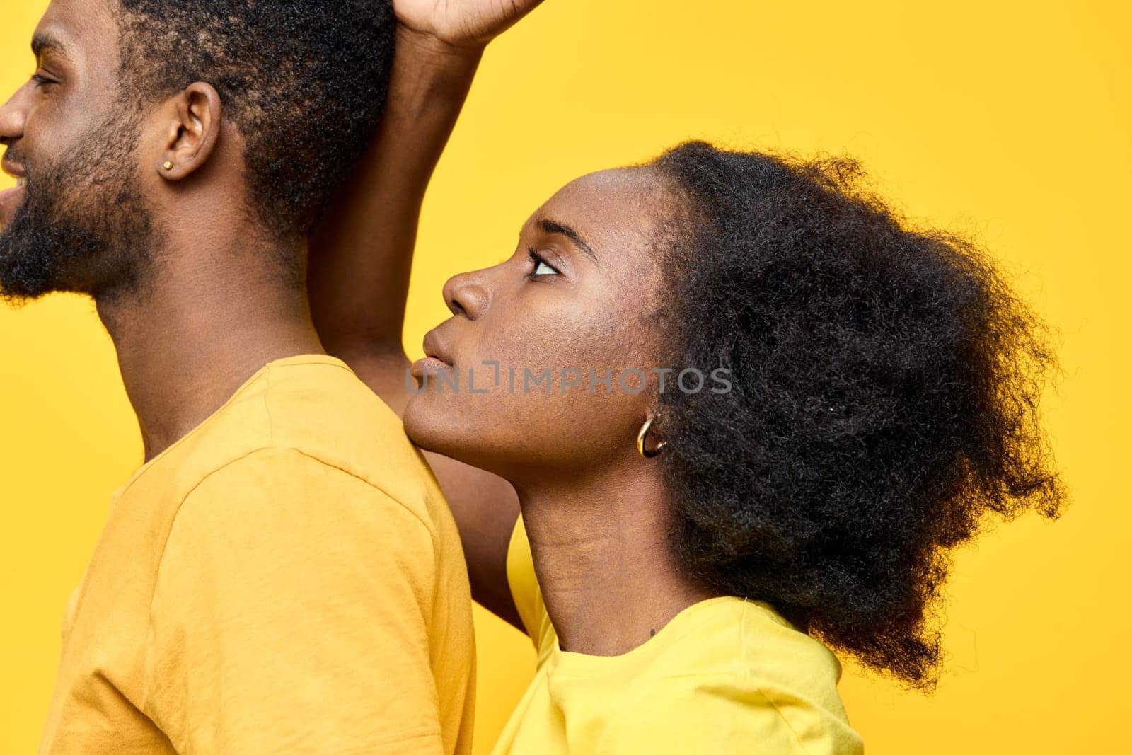 This vibrant image features a young Black couple with natural hairstyles, dressed in matching yellow outfits Set against a bright yellow background, the photo conveys emotions of love and connection