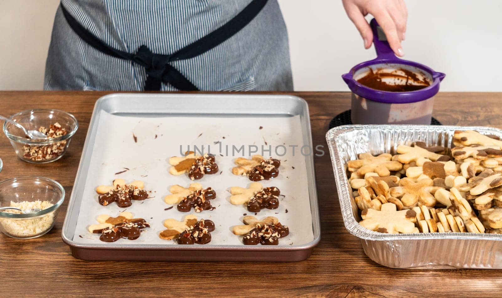 Creating snowflake-shaped cutout sugar cookies, dipped in chocolate, and adorned with crushed pecan nuts, elegantly presented on parchment.