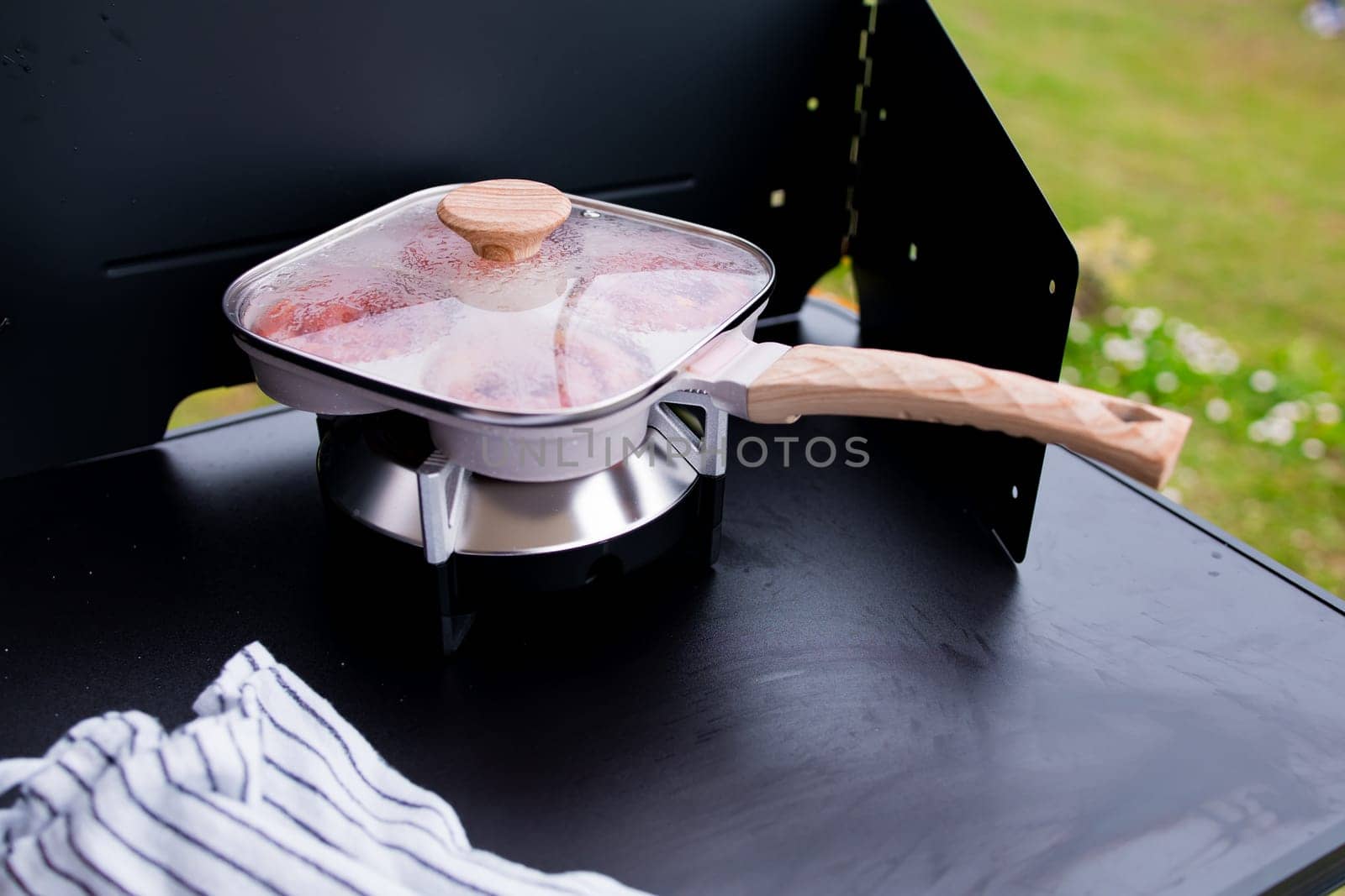 Square pan with wooden handle on stove outdoors.