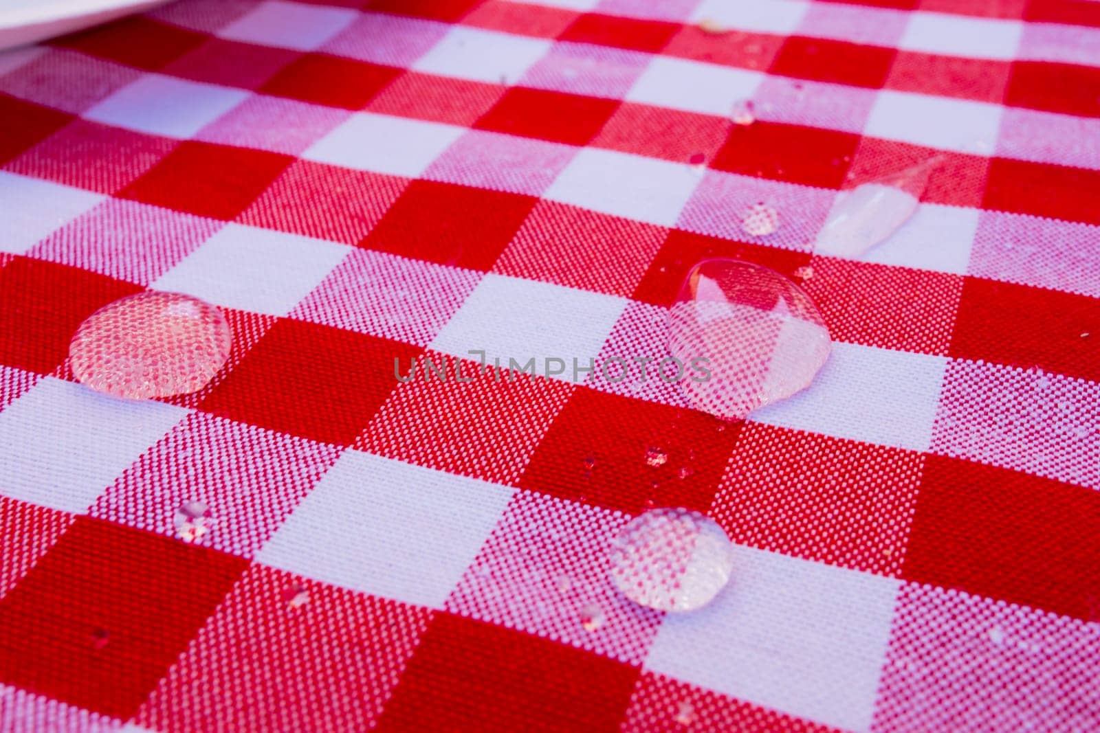Red and white checkered tablecloth with water droplets in close up view.