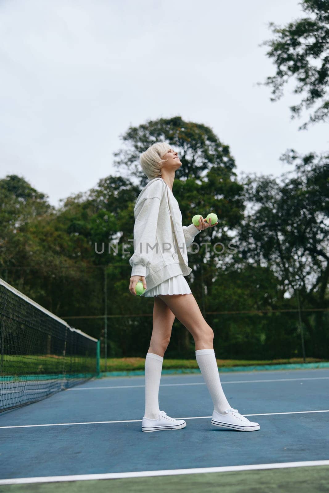 Energetic young female athlete in stylish sports attire holding weights on a tennis court, surrounded by greenery, conveying themes of health, fitness, and determination