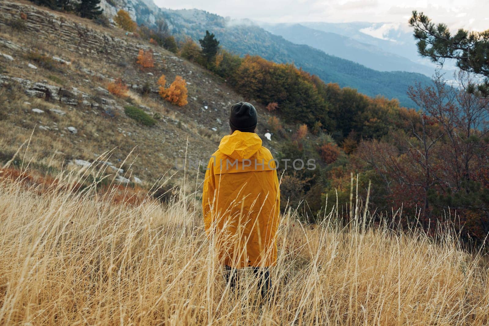 A person in a yellow coat enjoying the serene beauty of nature with majestic mountains in the background