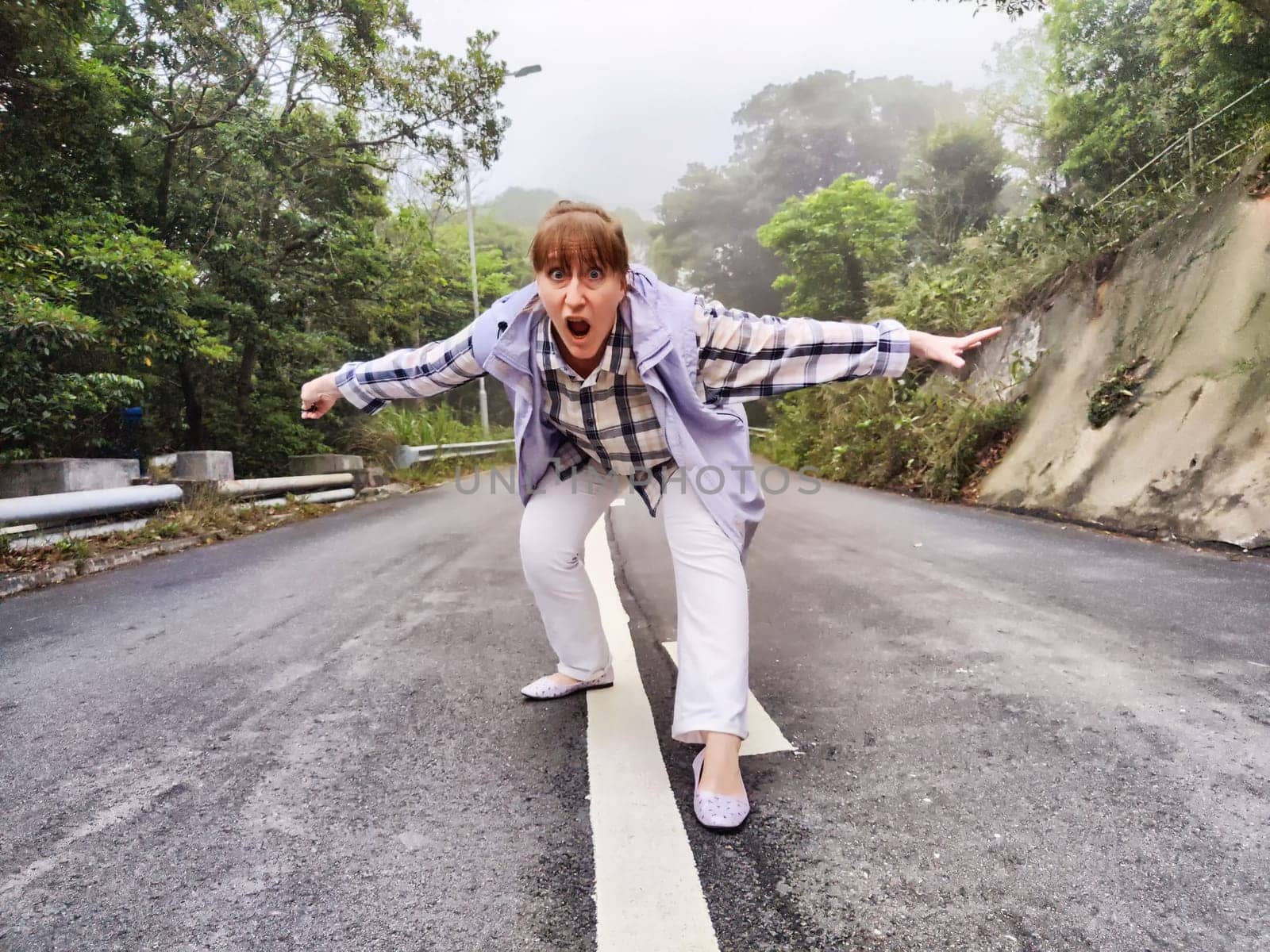 Blonde woman joyfully poses on a deserted road surrounded by fog, showcasing her adventurous spirit as a lifestyle blogger.