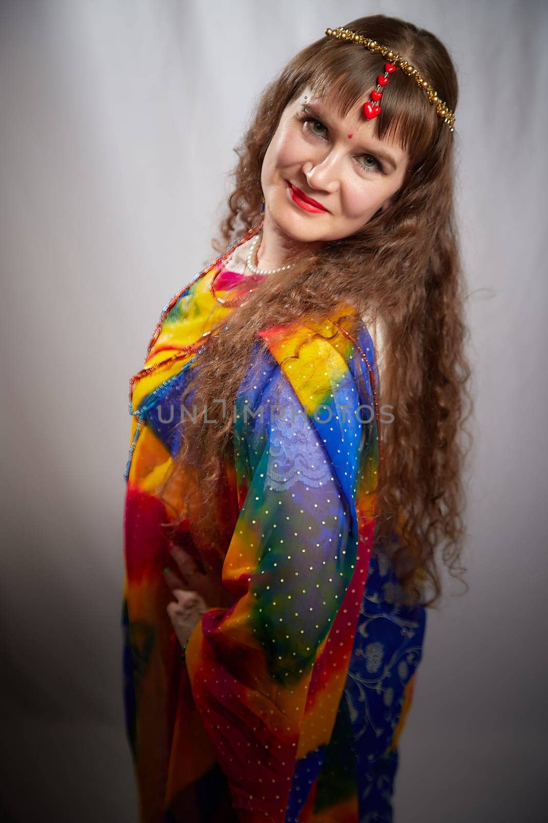 A mature woman in a colorful sari poses confidently, showcasing traditional Indian fashion during a creative photoshoot in a studio setting.