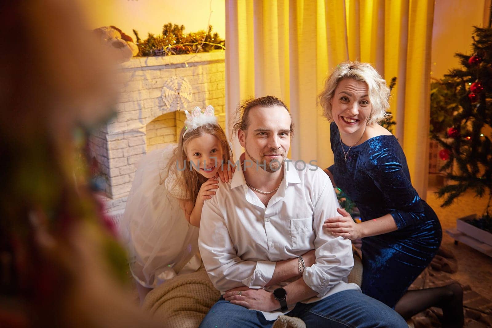 A family enjoys holiday festivities, posing together in front of a decorated fireplace and Christmas tree, radiating joy.