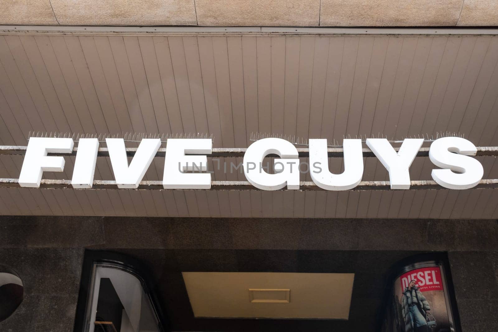 Milan, Italy - April, 08, 2025: Five Guys fast food restaurant storefront sign in bold white letters on metal frame. Street-level entrance exterior view.