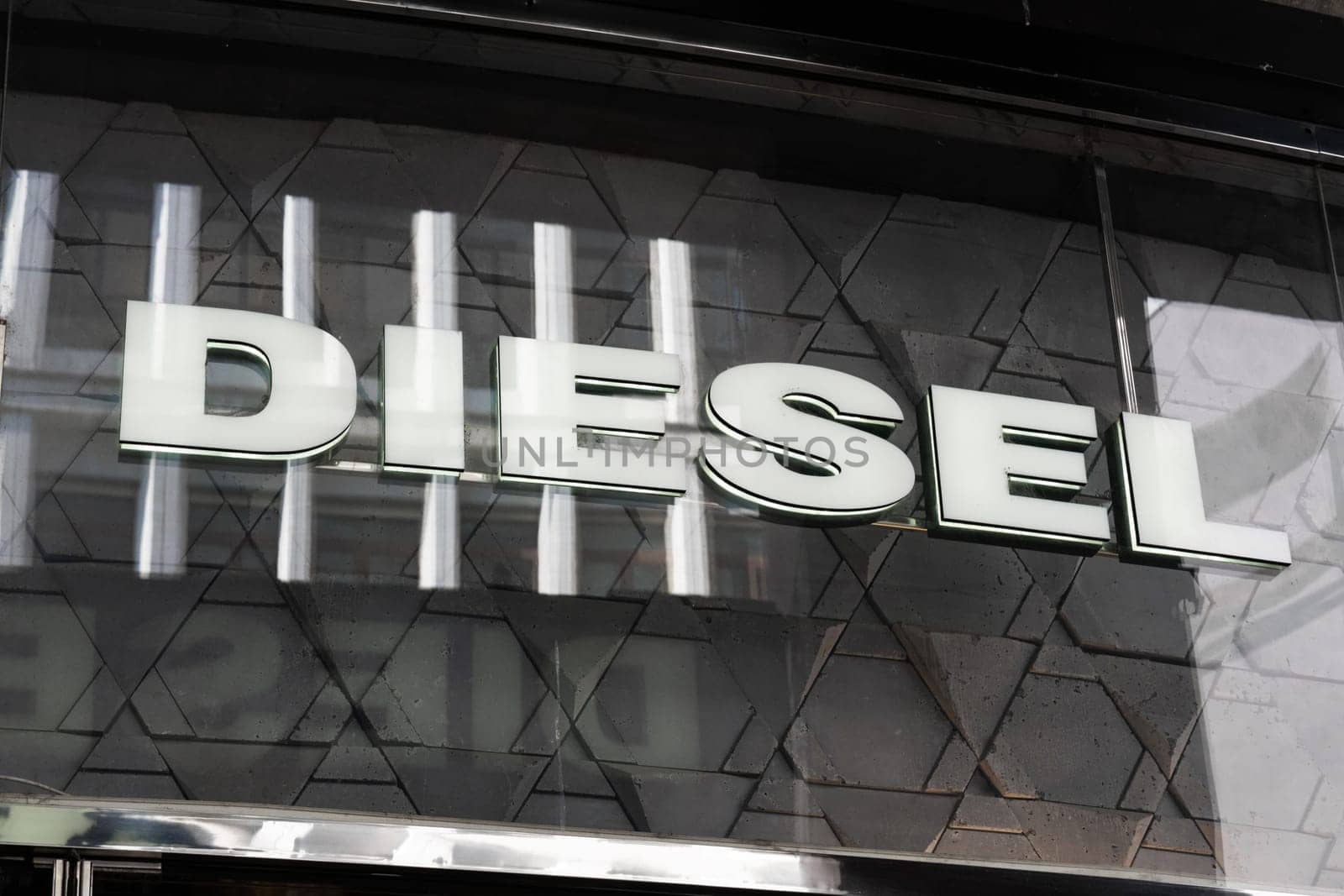 Milan, Italy - April, 08, 2025: Diesel illuminated logo sign on store facade. Brand signage on modern exterior glass with geometric tile reflection details.