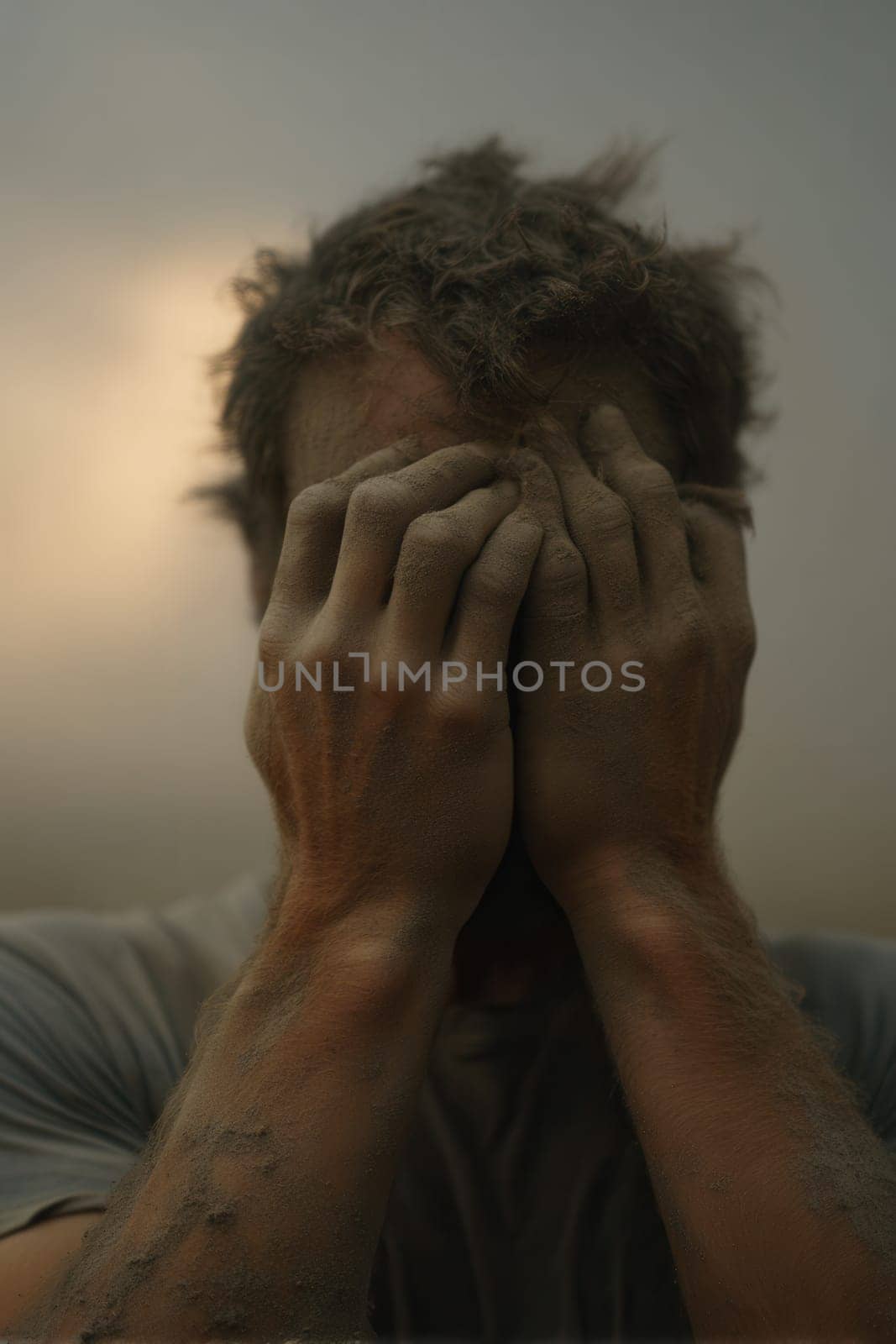 Man in despair with face and arms covered in dust, hiding his expression with both hands. A powerful visual for stories about disaster aftermath, human resilience, trauma, or mental health