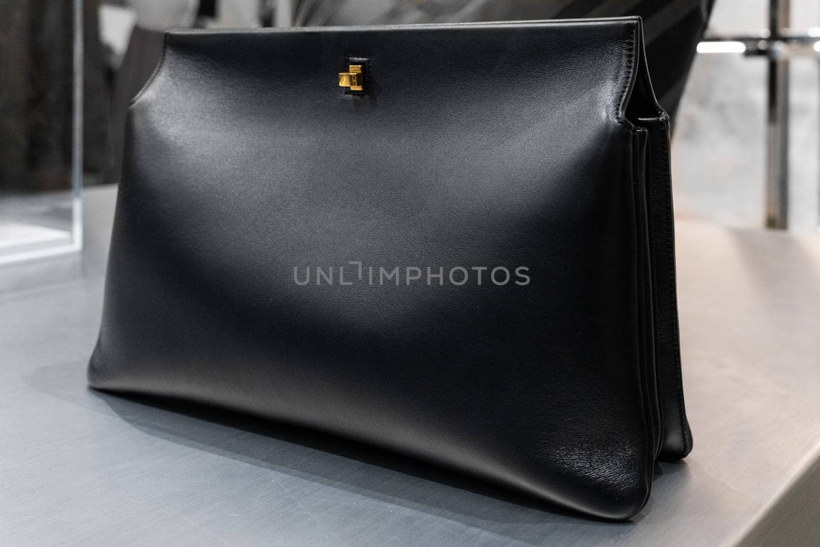Milan, Italy - April, 08, 2025: Black leather Phoebe Philo clutch bag with gold clasp detail on display inside boutique store. Luxury accessories, close up product view.