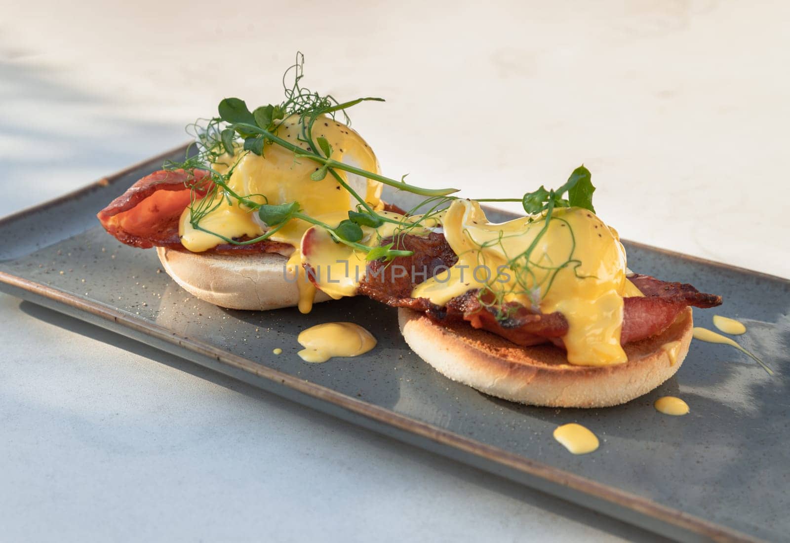 Eggs Benedict made with english muffin, grilled bacon, a brace of poached hen's eggs & hollandaise sauce and watercress served on ceramic tray. use it as your Wallpaper, Poster and Space for text, Selective focus.