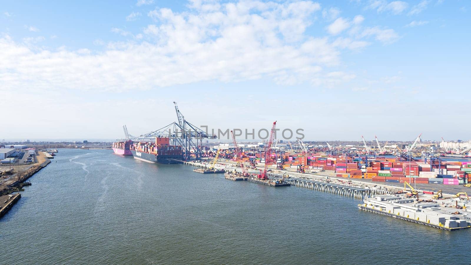 New York NY USA - 09.02.2024: Cargo containers stacked in a shipping yard near the sea with a city in the background.