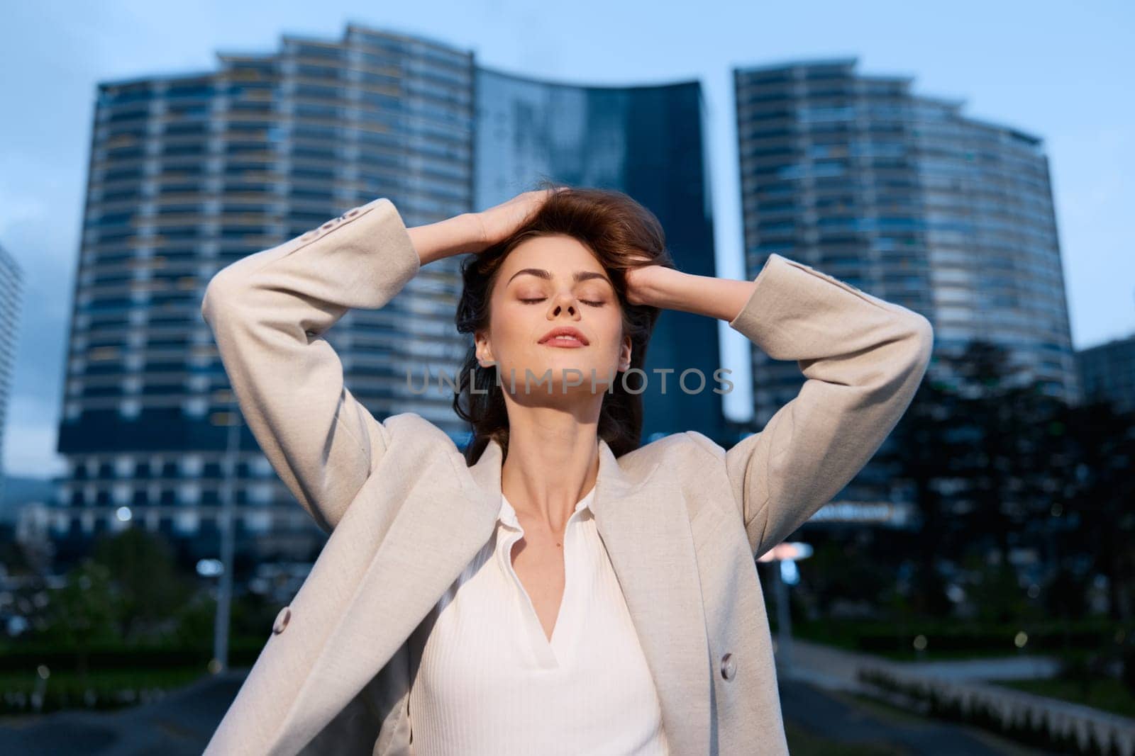 A poised woman in a professional outfit, taking a moment of reflection outdoors amidst contemporary buildings, symbolizing success and ambition in her career.