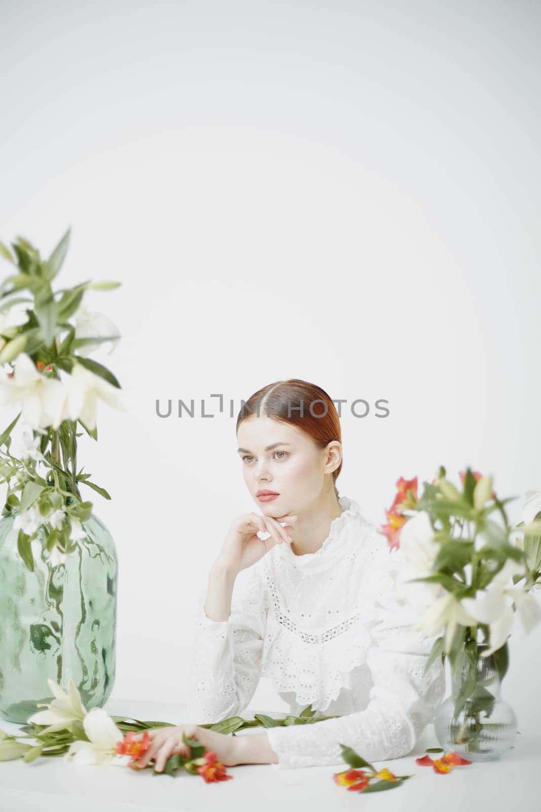 A serene portrait of an elegant woman in a white lace blouse, surrounded by colorful flowers in glass vases, expressing beauty and tranquility in a minimalistic setting