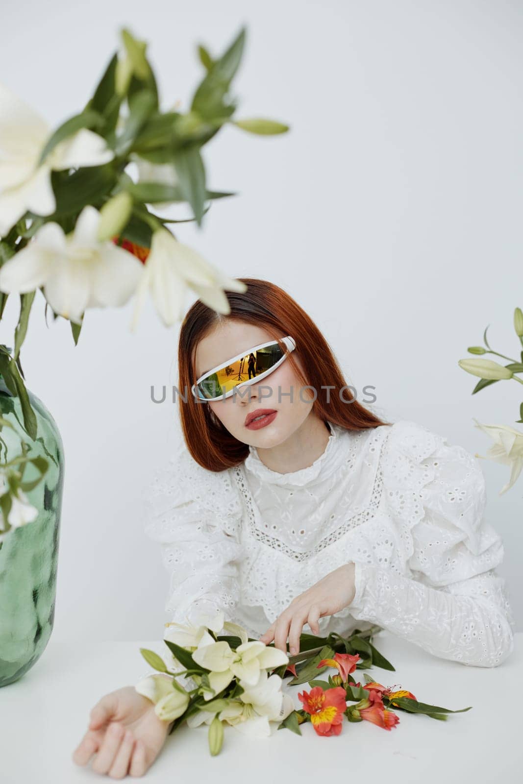 Modern woman in chic sunglasses surrounded by vibrant flowers on a clean white backdrop, evoking a sense of freshness and elegance in springtime