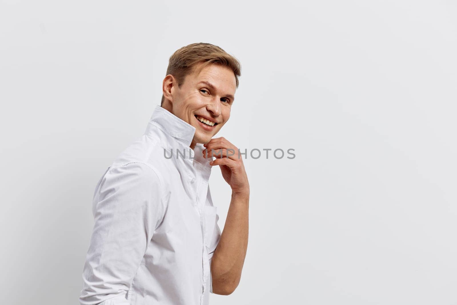 Relaxed young man with a bright smile, dressed in a white button-up shirt, standing against a plain white studio backdrop. He appears confident and approachable, conveying positivity and friendliness. Concept: casual professionalism.