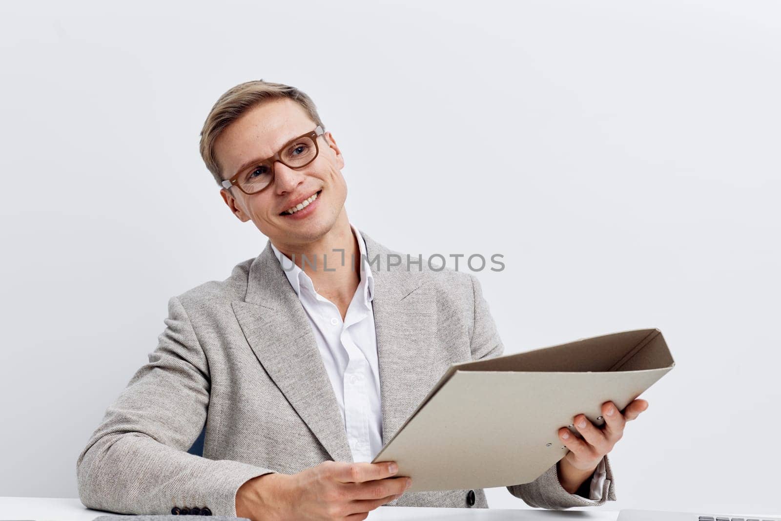 Smiling businesswoman with short hair and glasses, dressed in a light gray blazer and white shirt, holding a folder in her hands. Bright office environment, positive mood, professional appearance, corporate attire, success concept, modern work setting.