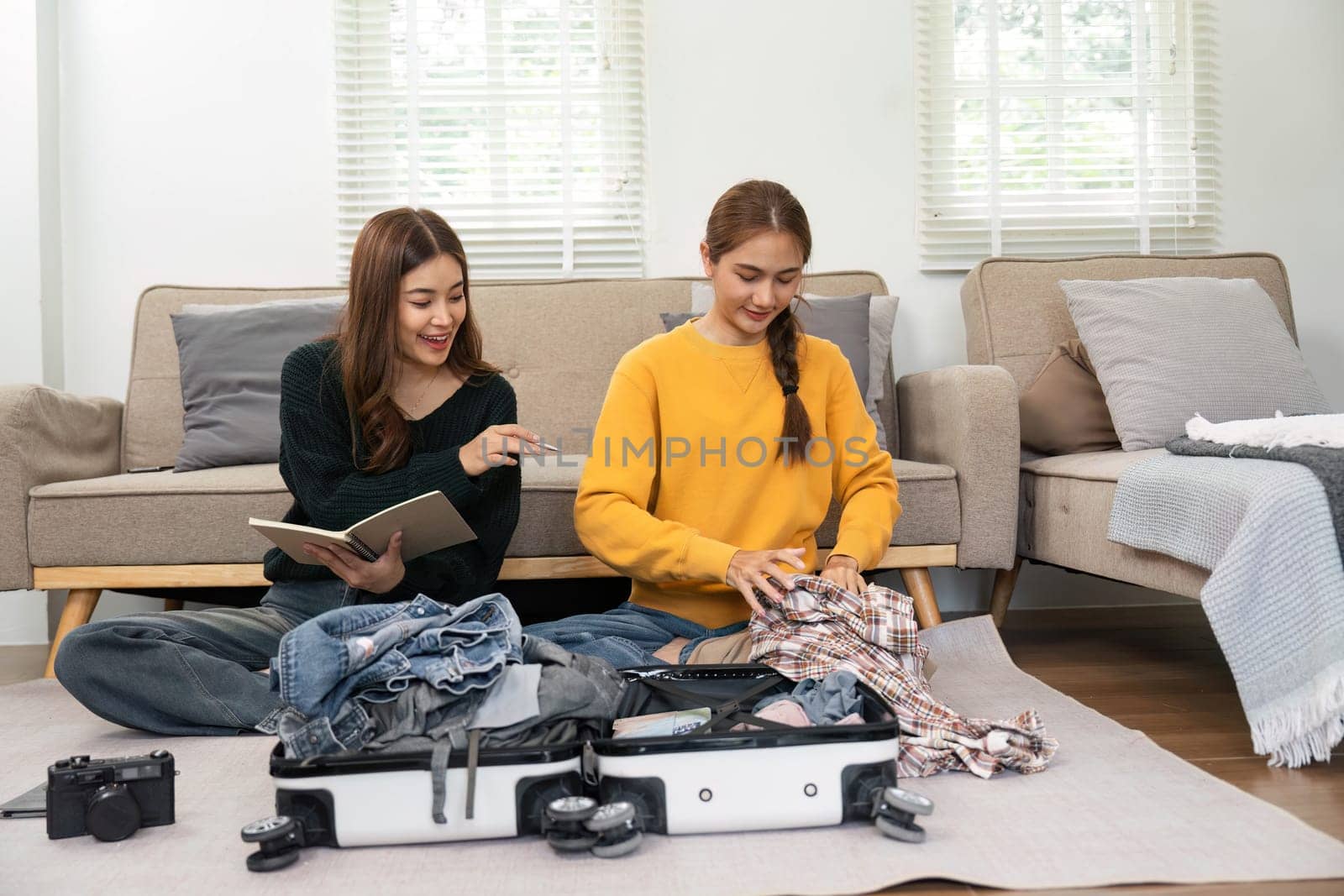 Two young women sharing laughter and conversation while packing clothes into a suitcase, readying for their exciting journey.