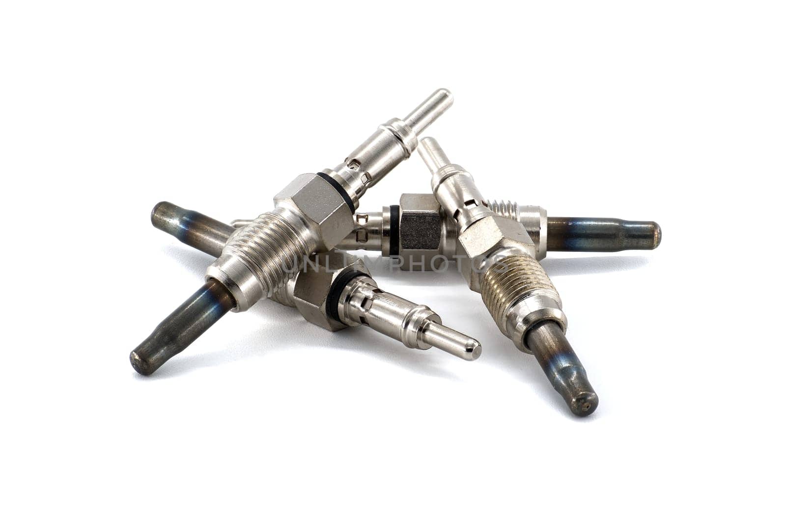 An assortment of metallic glow plugs for diesel engines arranged on a white surface. Essential components for cold-starting diesel vehicles.