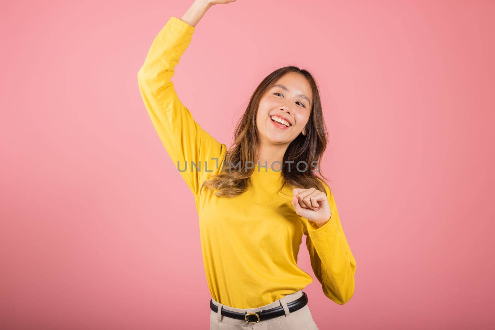 Asian young woman dancing with inspired face expression and raising hands up, Portrait of happy female model jocund in sneakers dancing, studio shot isolated on pink background, Time to relax