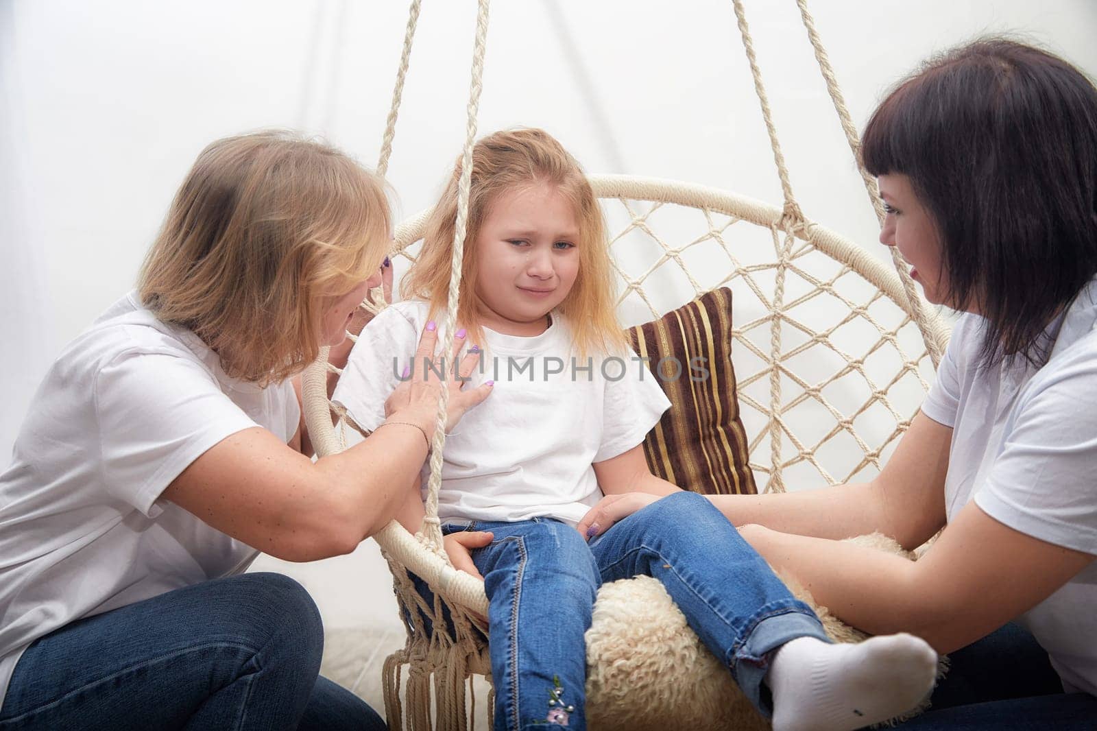 In a nurturing environment, an adult comforts a child on a swing seat while another adult engages in supportive conversation.