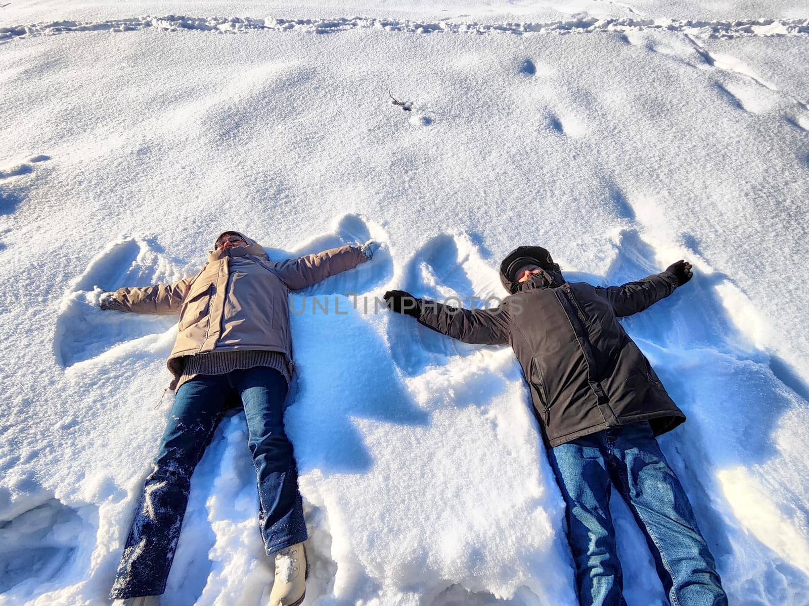 Friends enjoy a playful winter day as they lie on the snow and create snow angels, surrounded by a bright and clear blue sky, showcasing the joy of the season.