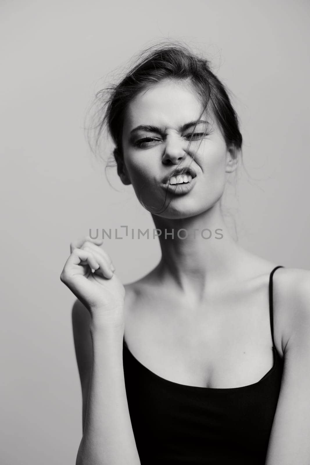 Playful young woman with messy hair making a funny face and clenched fist, evoking a sense of joy and spontaneity in a minimalist black and white setting.
