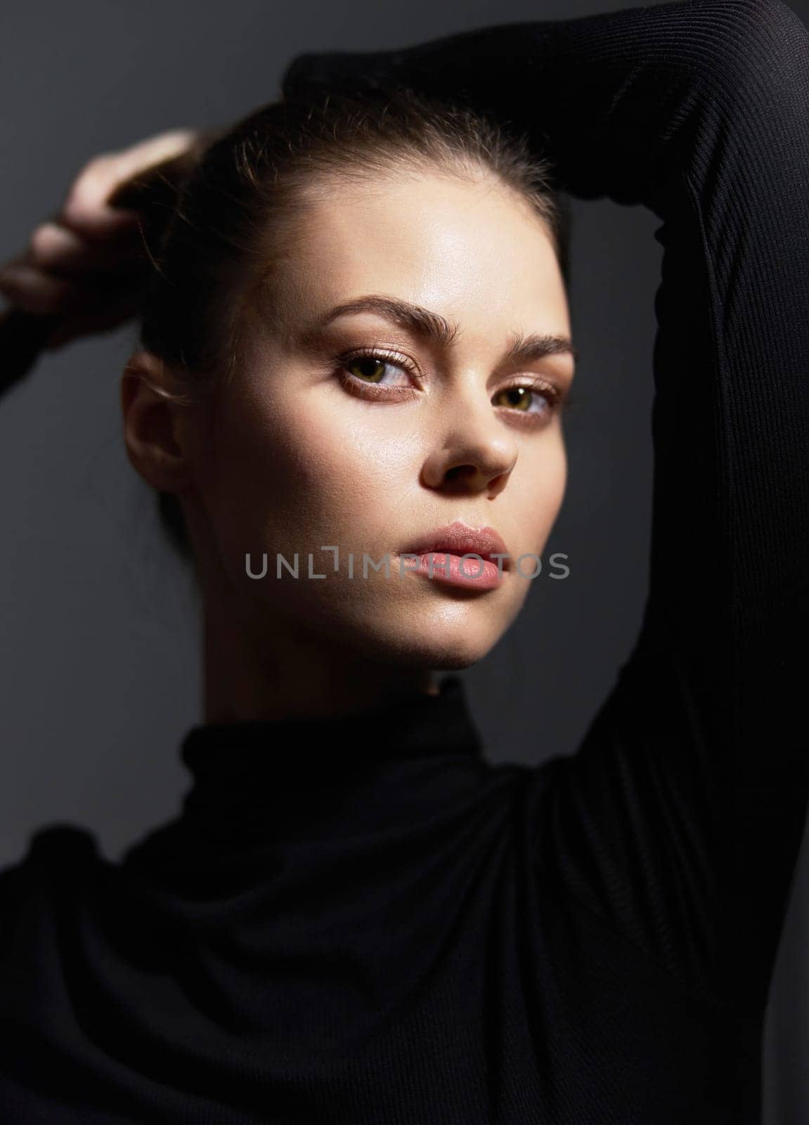 Portrait of a beautiful young woman showcasing elegance and confidence, her hair styled back, against a moody dark backdrop. Emphasizes fashion and modern beauty.