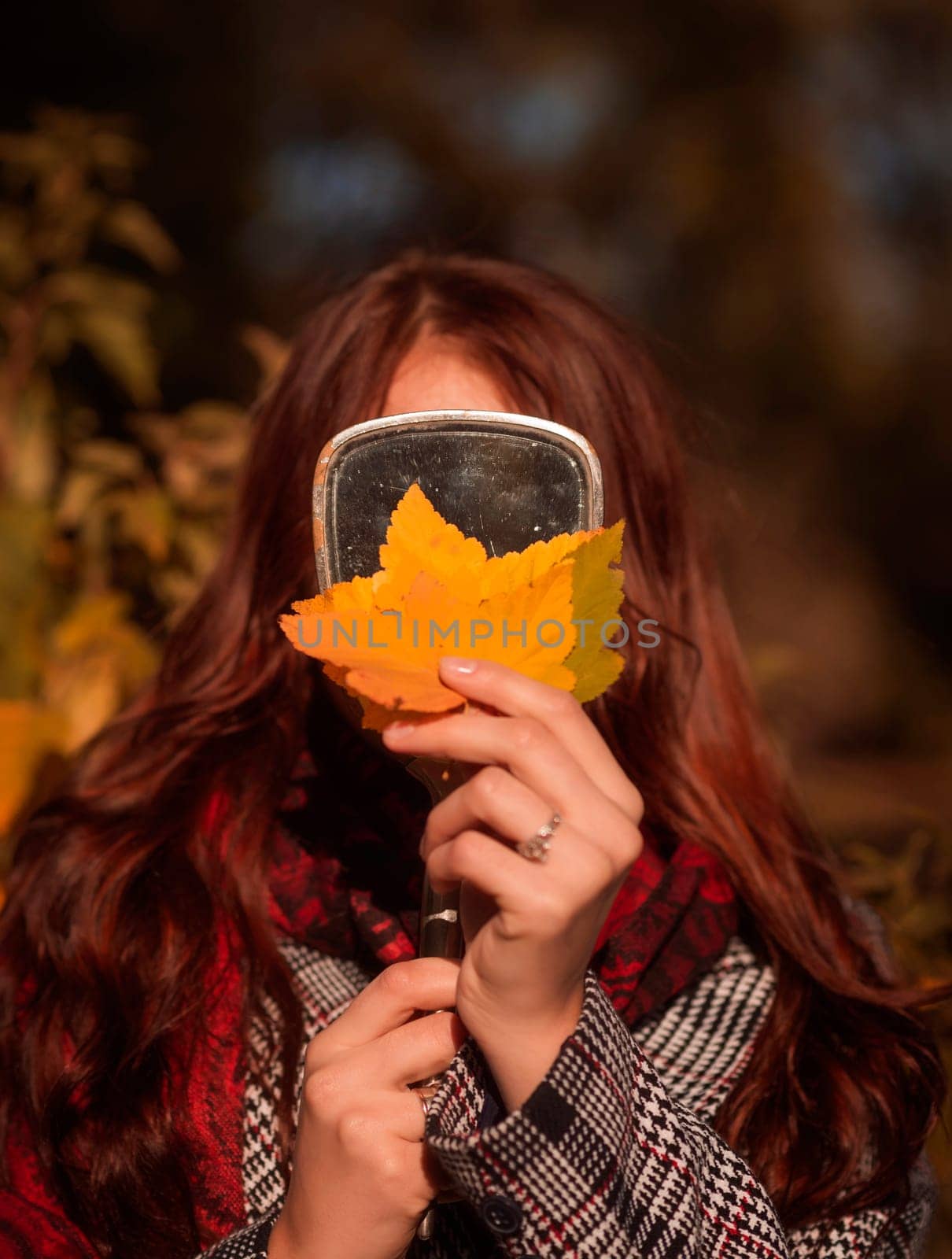 young girl holding yellow autumn leaves in her hands against the background of a mirror. autumn concept. she is wearing a coat. her face is not visible