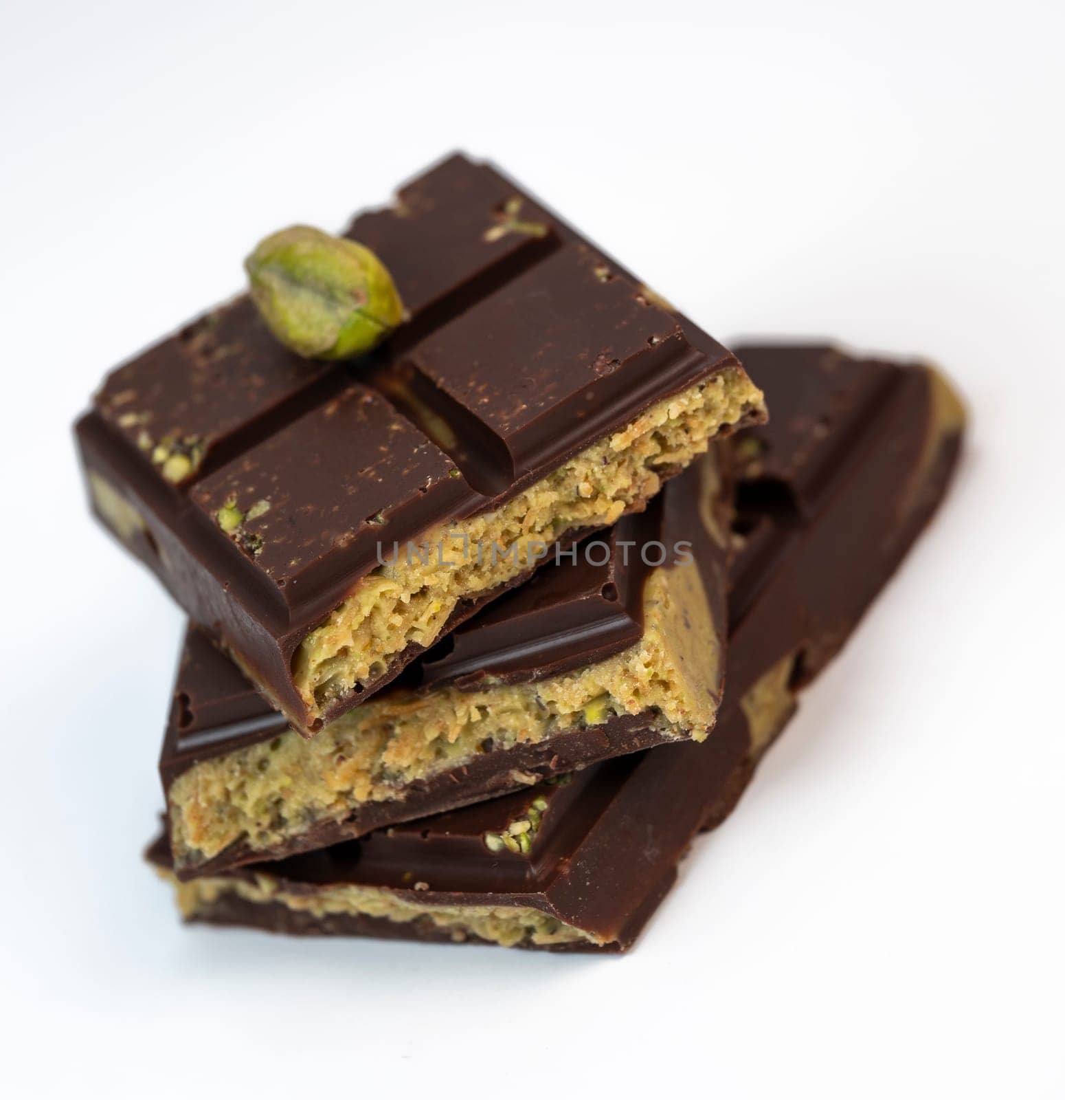Stacked layers of kadaif embrace a generous coating of rich chocolate and are topped with a pistachio, showcasing the delightful texture and flavors in a culinary presentation.