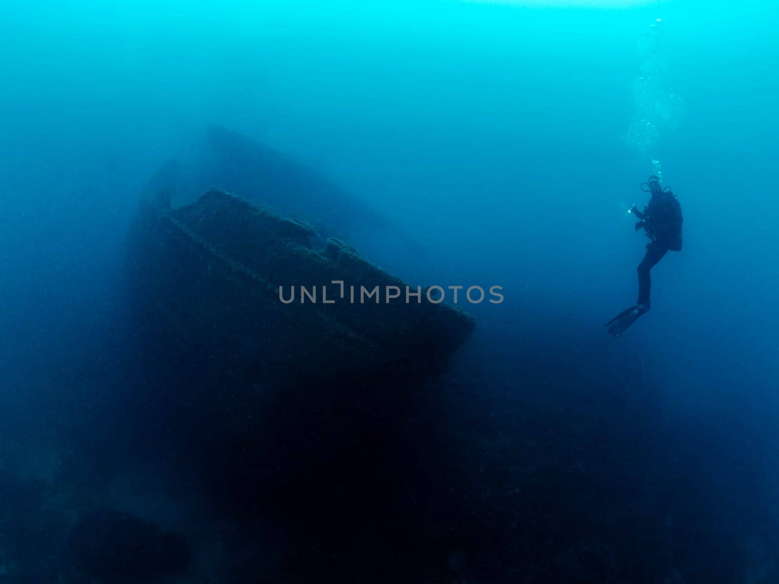 diver diving in front of the remains of a sunken ship in the blue ocean, concept of underwater adventure and active leisure lifestyle, copyspace for text