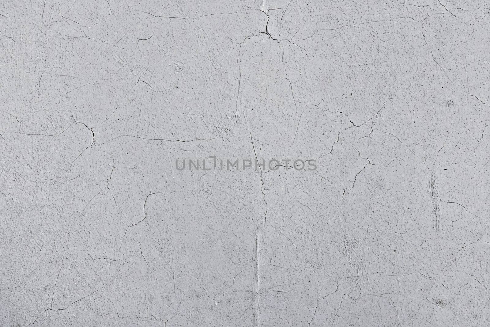 A gray surface displays a textured appearance with varying cracks and imperfections. This minimalist backdrop showcases variations in color and texture, highlighting its raw aesthetic.