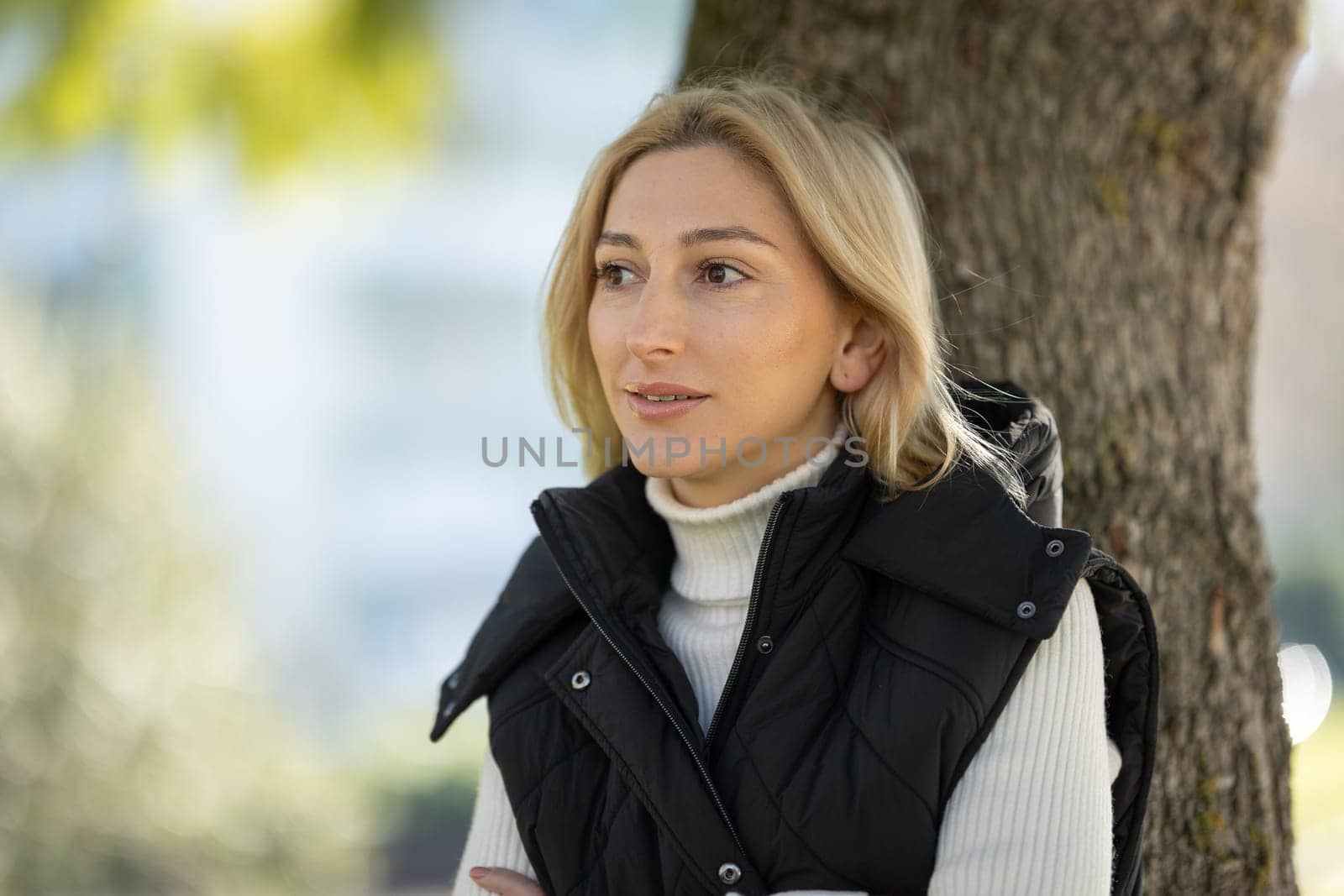 Young woman with crossed arms wearing black vest and white turtleneck is enjoying a relaxing day at the park