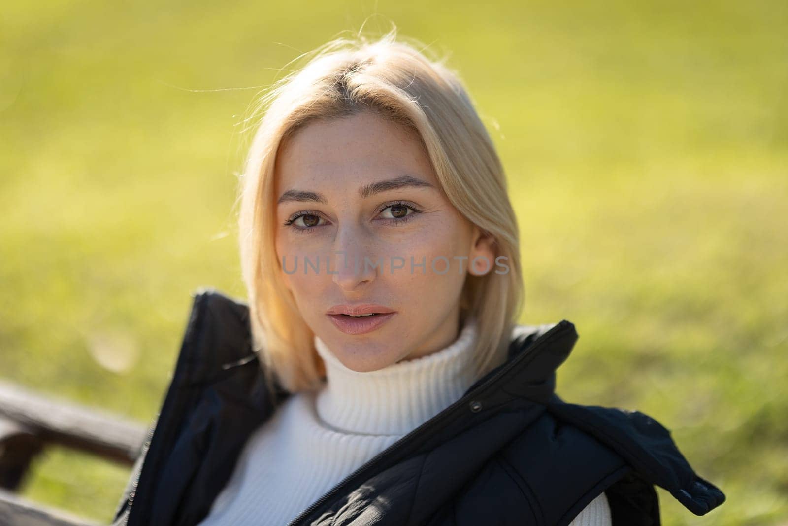 Blonde woman relaxing outdoors in nature wearing white turtleneck and black vest