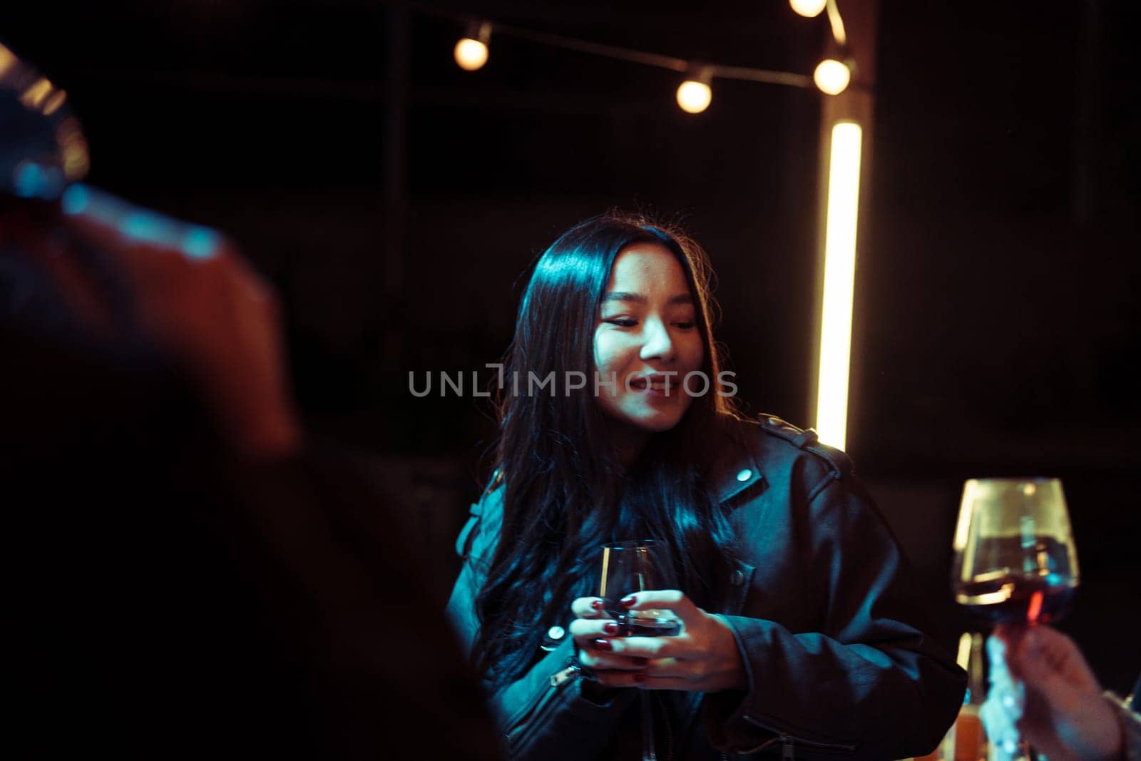 A group of friends enjoys a lively evening gathering, sharing drinks and smiles in a warm, inviting atmosphere illuminated by soft lighting. Laughter fills the air.