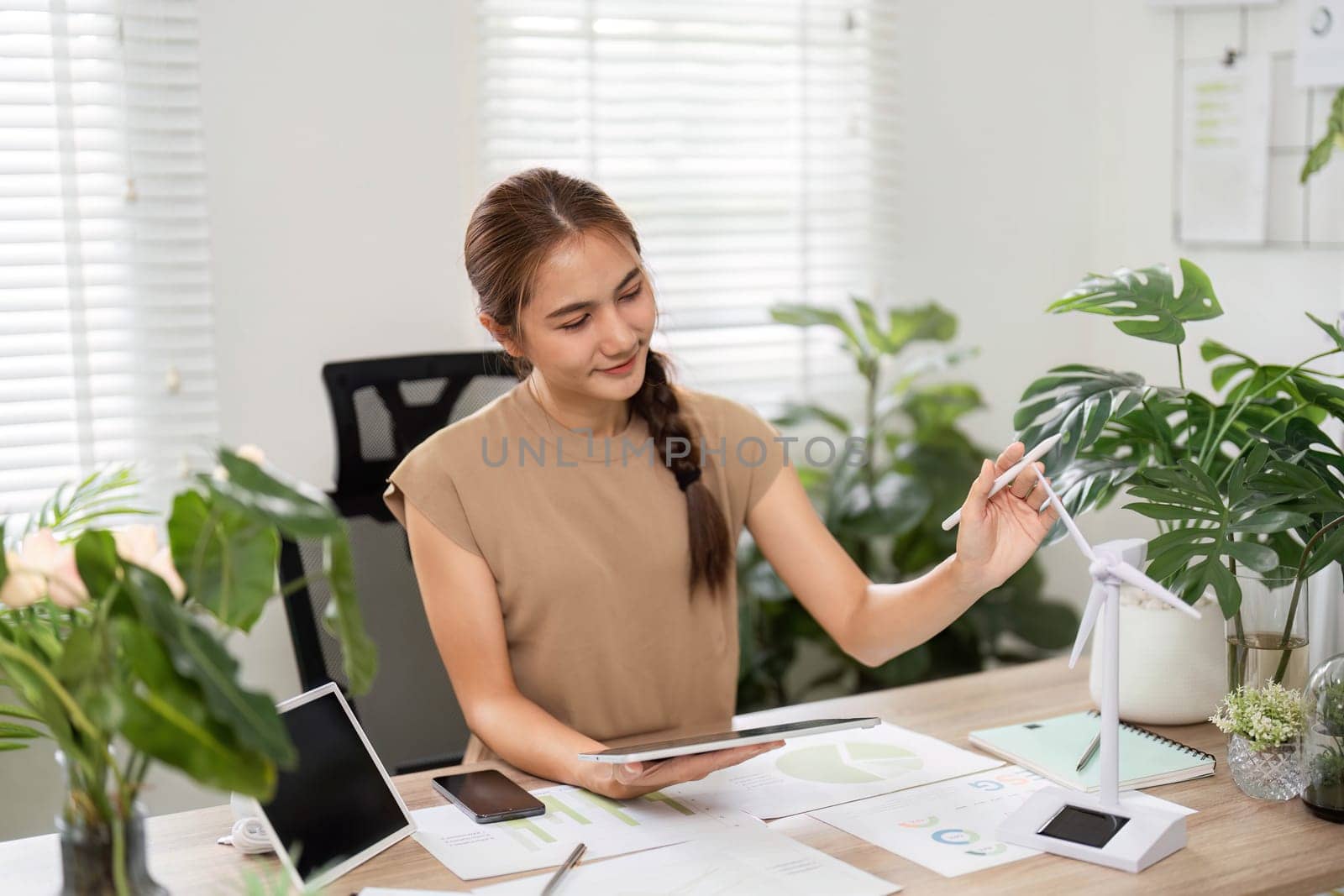 A woman analyzes data in a green office, focusing on ESG sustainability efforts with her tablet and thoughtful expression.