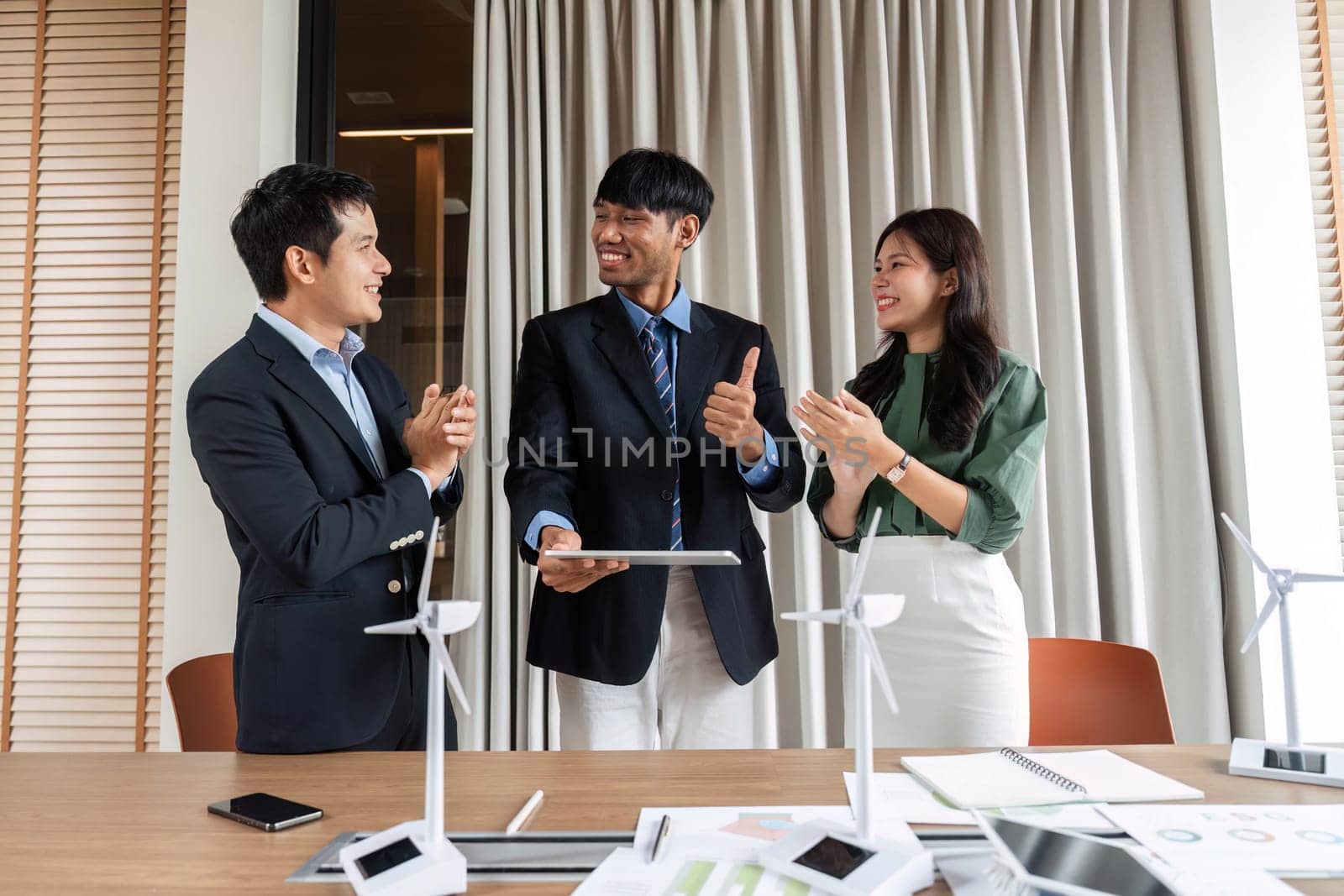 In a bright modern office, a diverse team celebrates successful ESG collaboration, expressing enthusiasm and positive energy after a productive meeting.