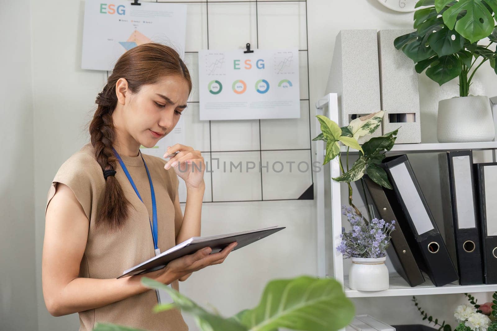A sustainability consultant thoughtfully reviewing ESG initiatives while standing in a modern office filled with greenery.