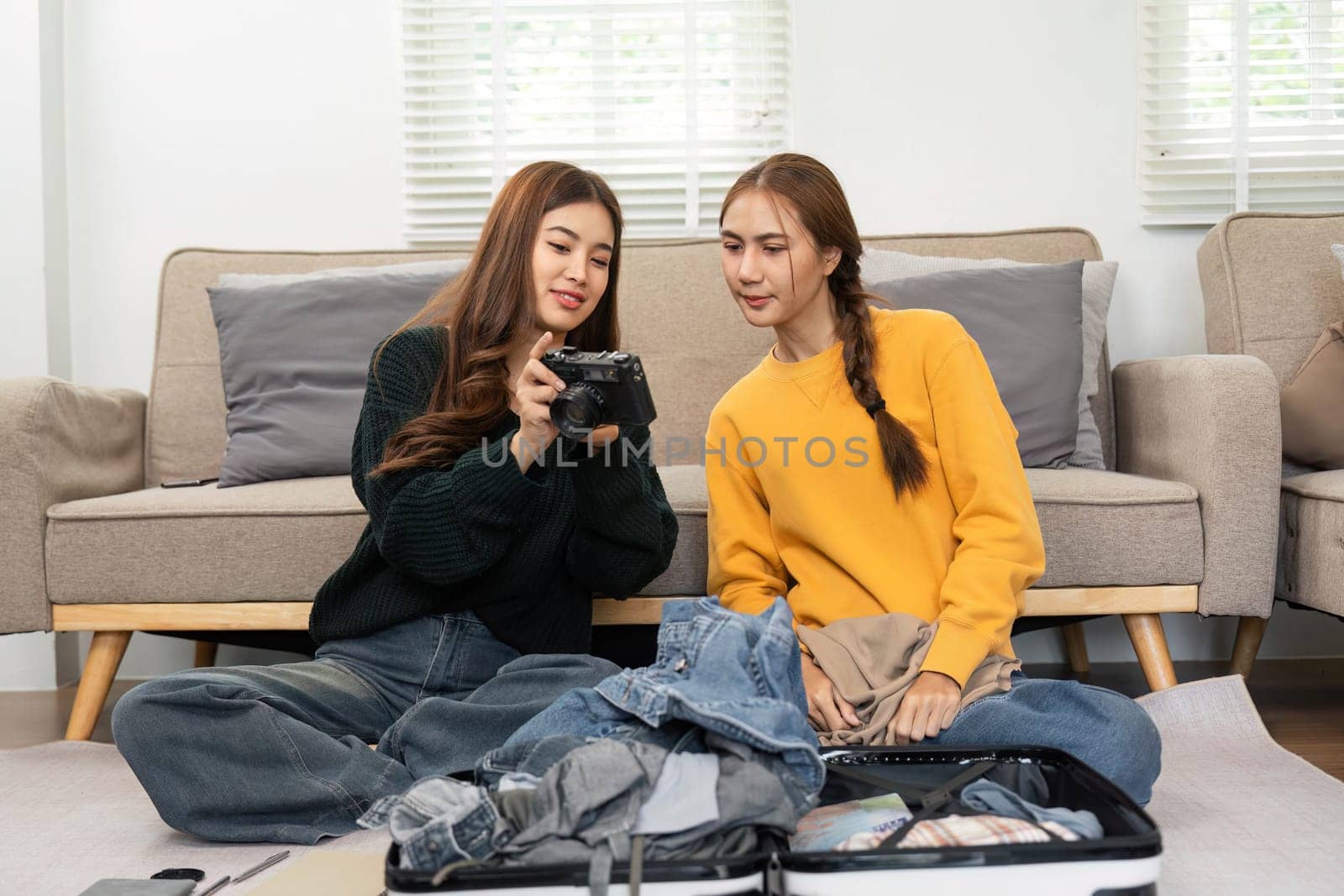 Two young women reviewing photos on a camera and discussing their travel plans while packing a suitcase, embracing friendship and adventure.