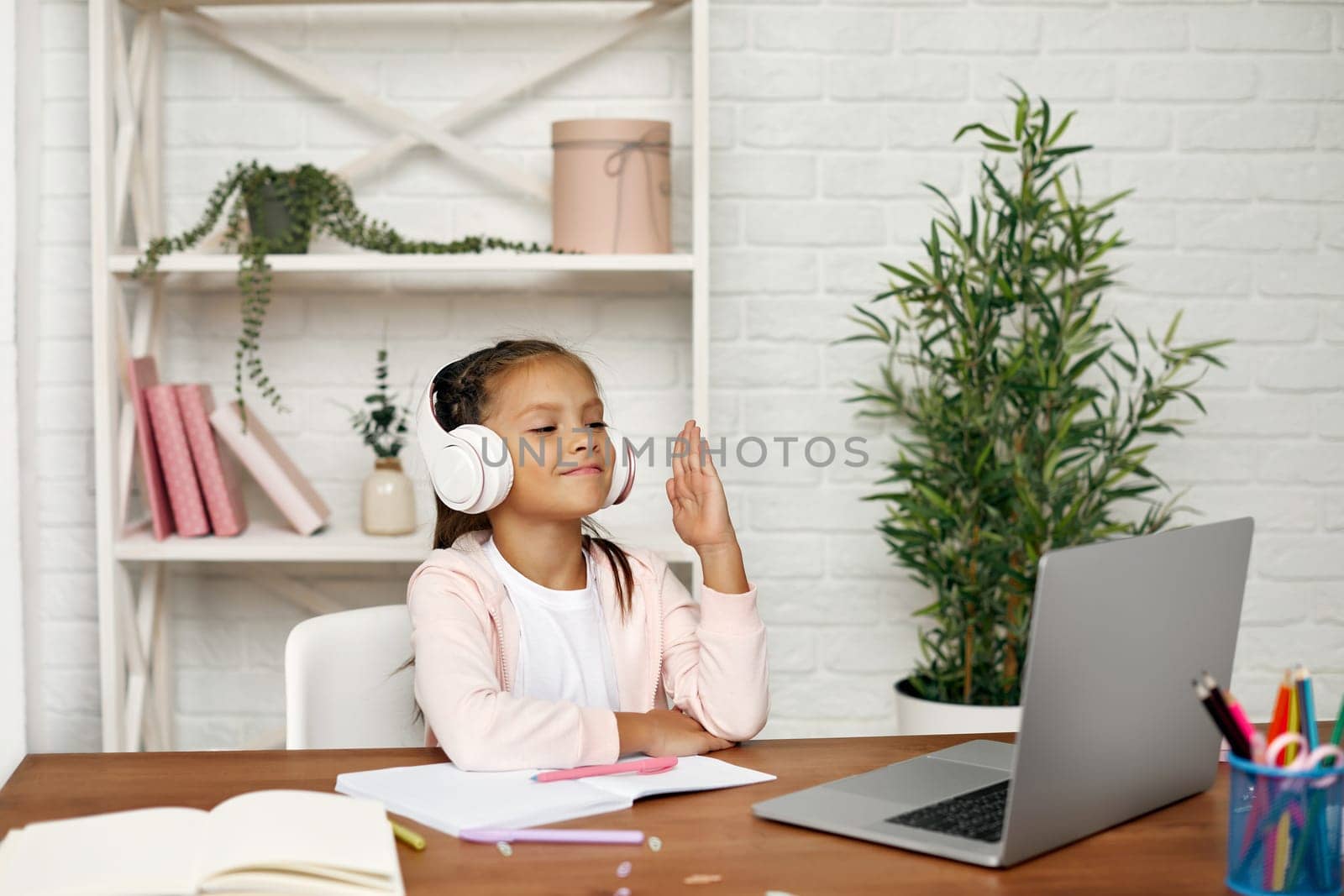 happy cute little child girl using laptop for studying online. child raises her hand to answer the teacher's question. online lesson at home