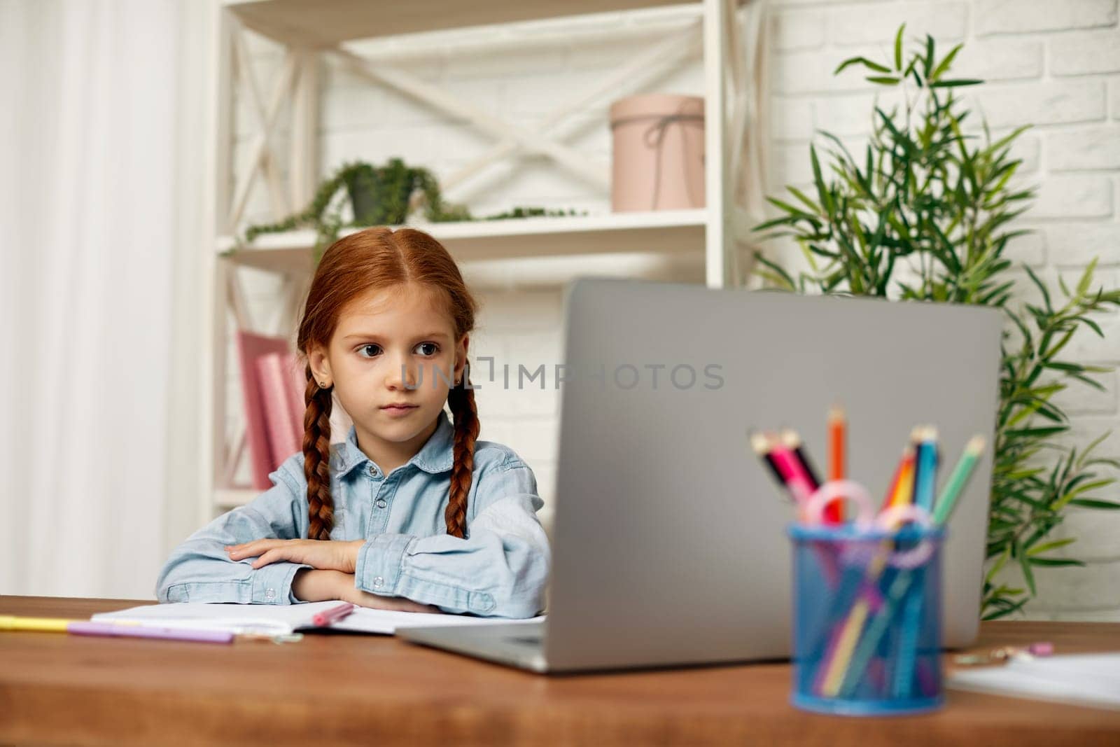 happy redhead little child girl using laptop for studying online learning system. online lesson at home