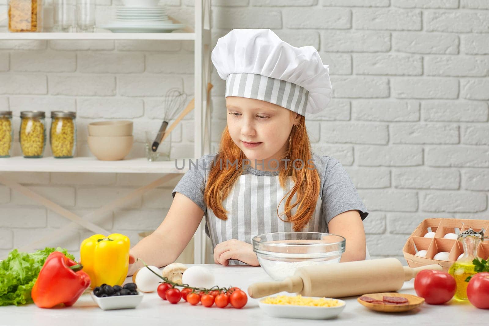 happy little girl in chef hat and an apron cooking pizza in the kitchen.