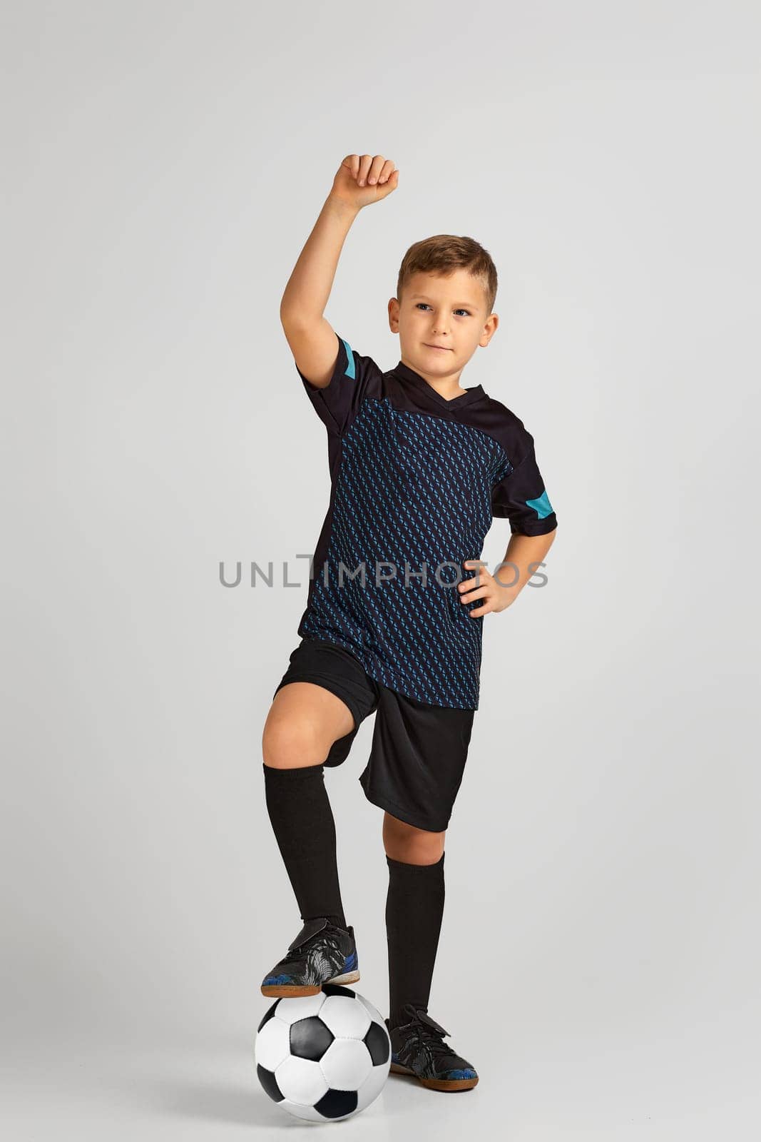 little boy football player in uniform holding his leg on ball over studio background. child dreams of becoming a soccer player.