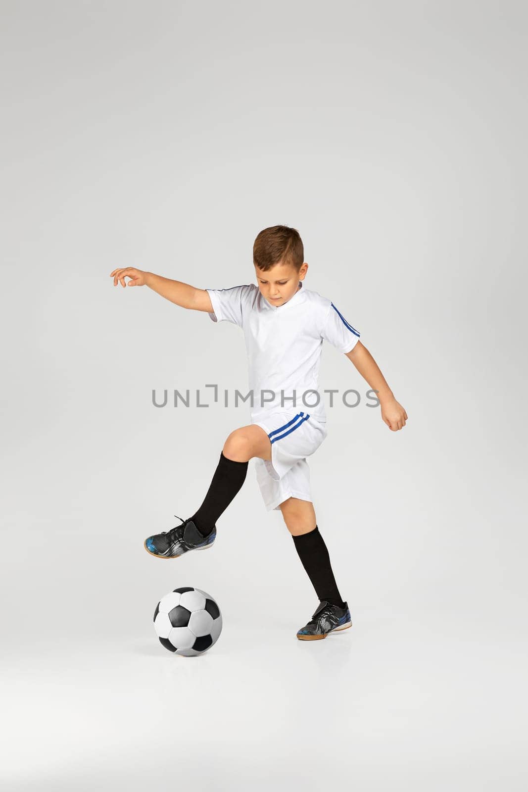 little child boy in uniform playing football over studio background.