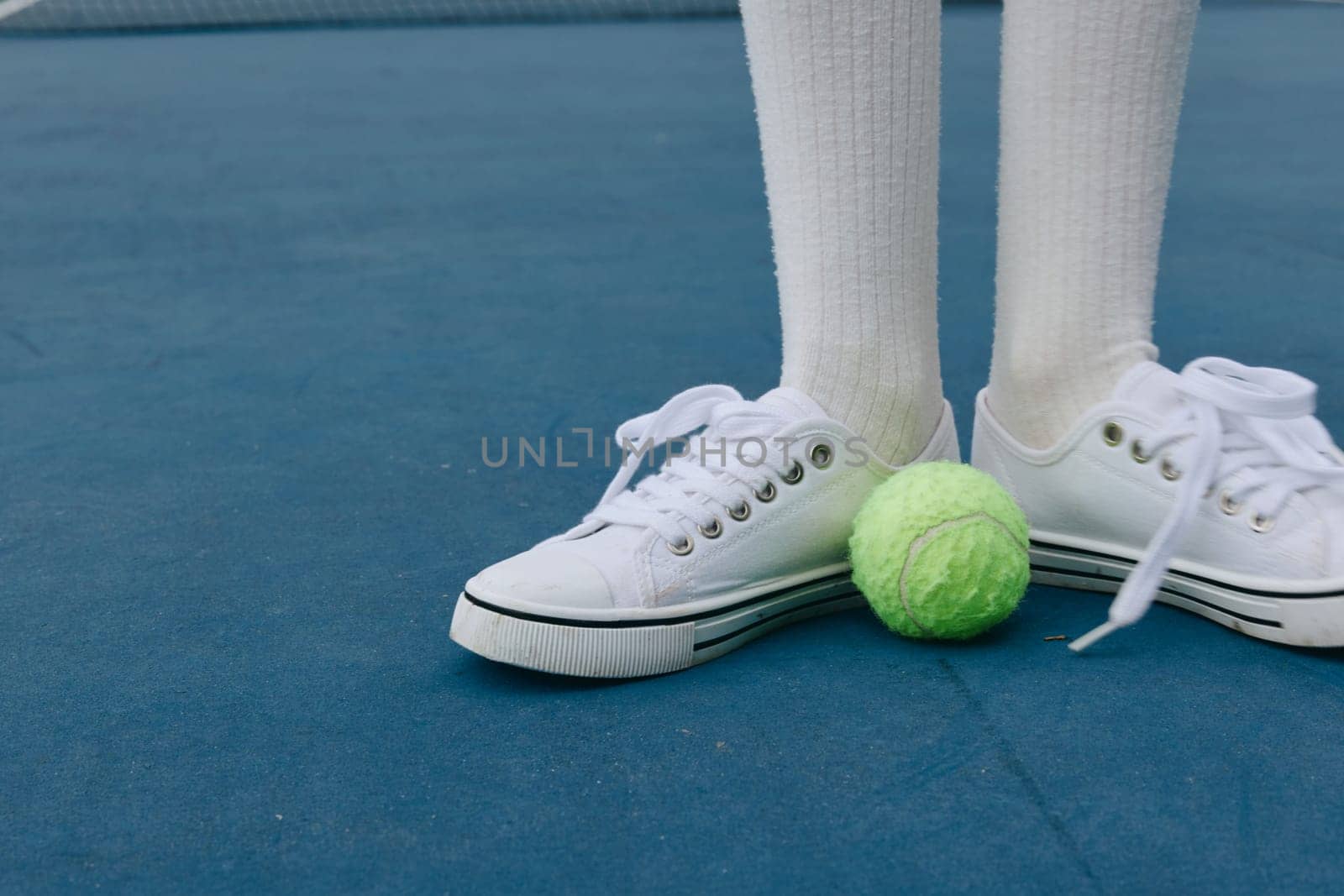 An energetic young athlete showcasing a sporty style on a blue tennis court, with a green tennis ball at their feet, capturing the essence of sports and fitness