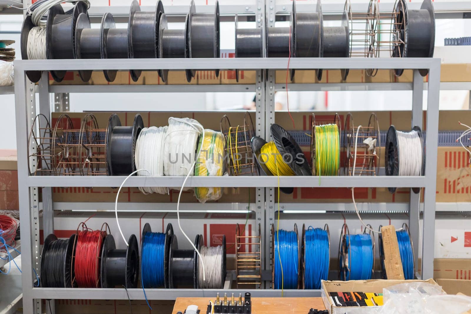 Spools of colorful electrical wires and cables are neatly organized on metal shelves in a warehouse, ready for use in various projects