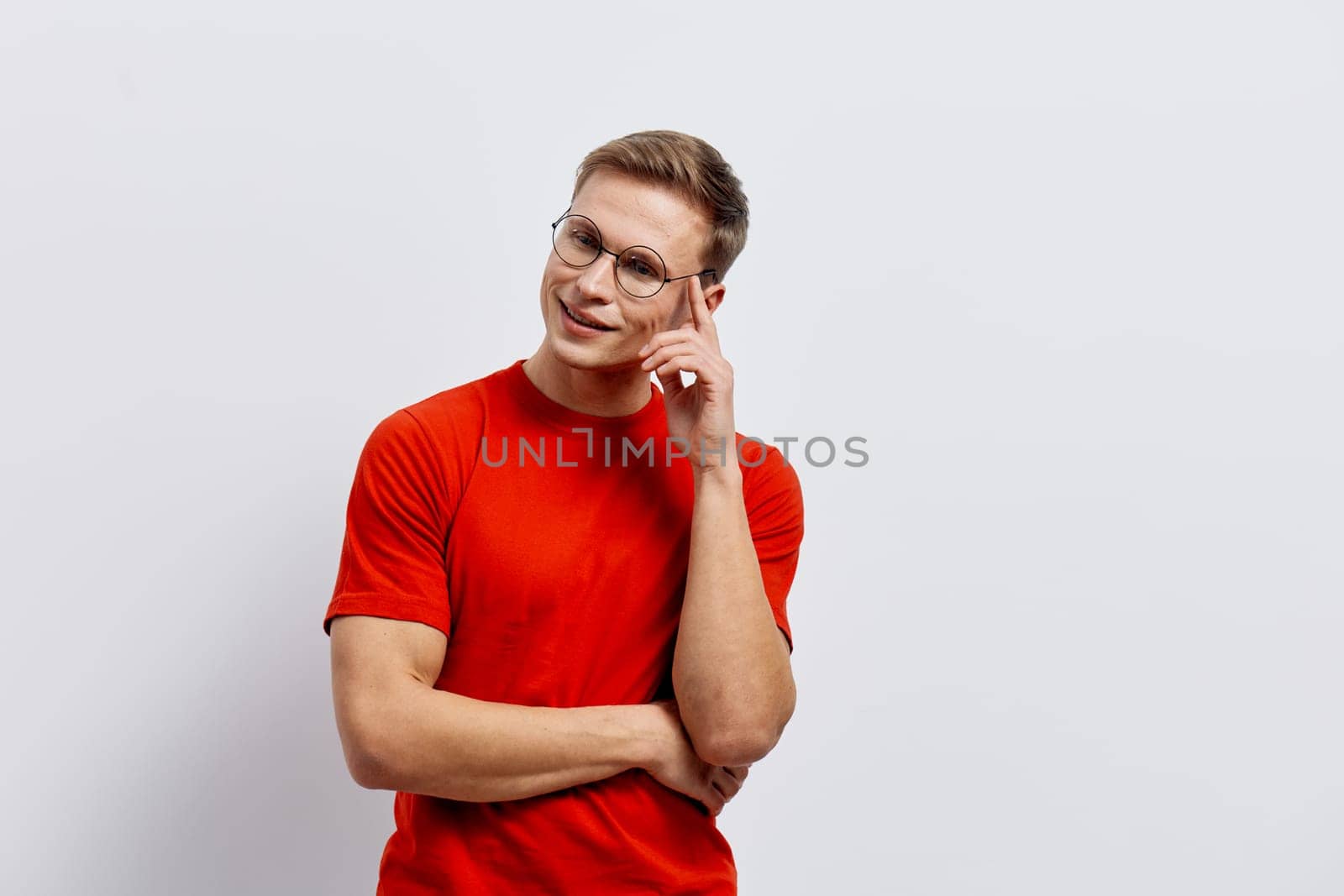 Happy woman with short brown hair, glasses, and a bright red casual t-shirt stands confidently with a smile, striking a thoughtful pose against a neutral background. This engaging portrait captures friendliness, confidence, and positivity, ideal for lifestyle, business, or communication themes.