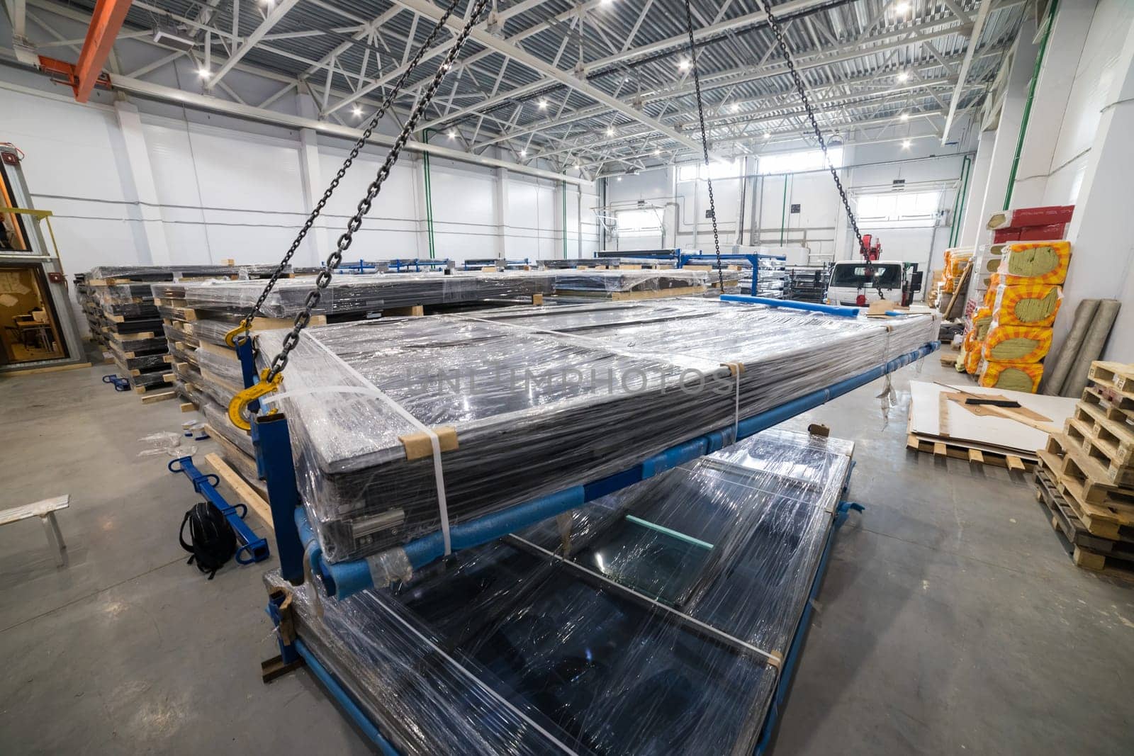 Crane lifting stack of solar panels inside warehouse, industrial production of photovoltaic panels