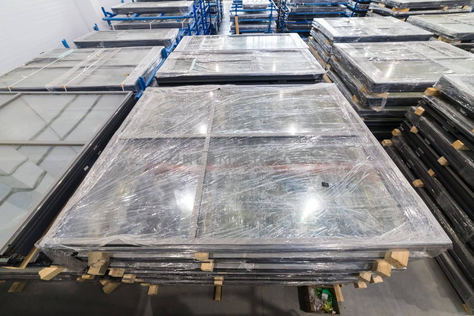 Large window frames wrapped in plastic film, stored in a warehouse, awaiting transportation to construction site or customer