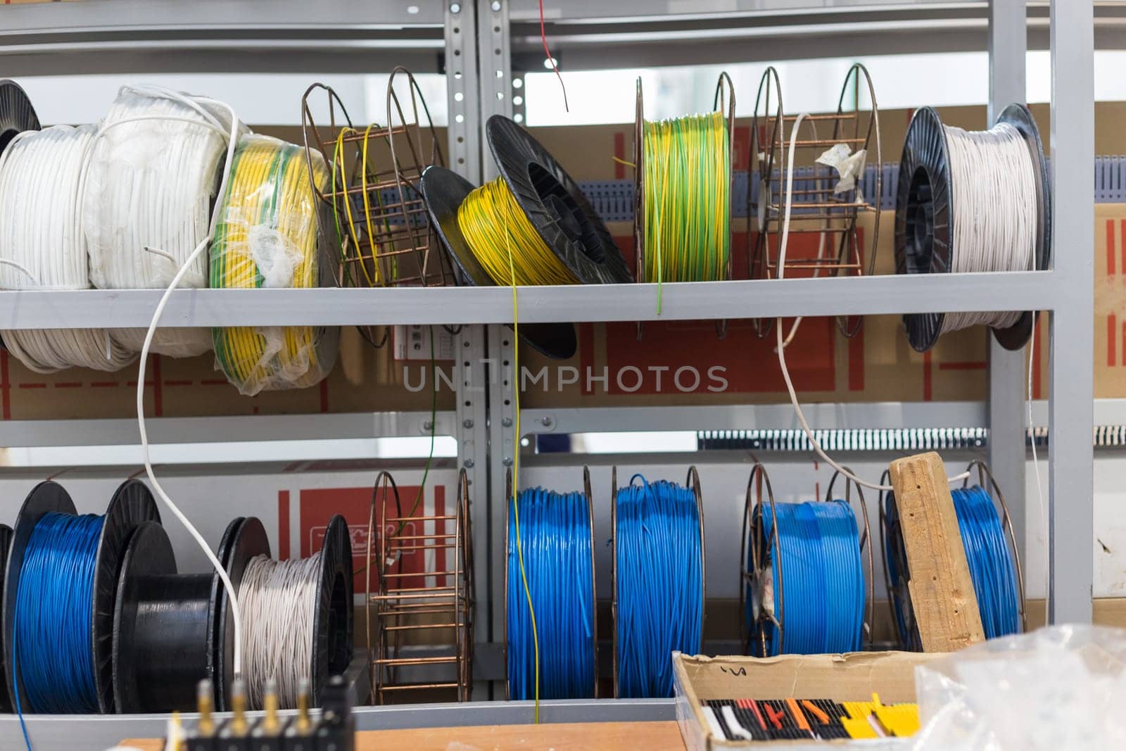 Spools of colorful electrical wires are neatly arranged on metal shelves in a warehouse, ready for use in various electrical projects