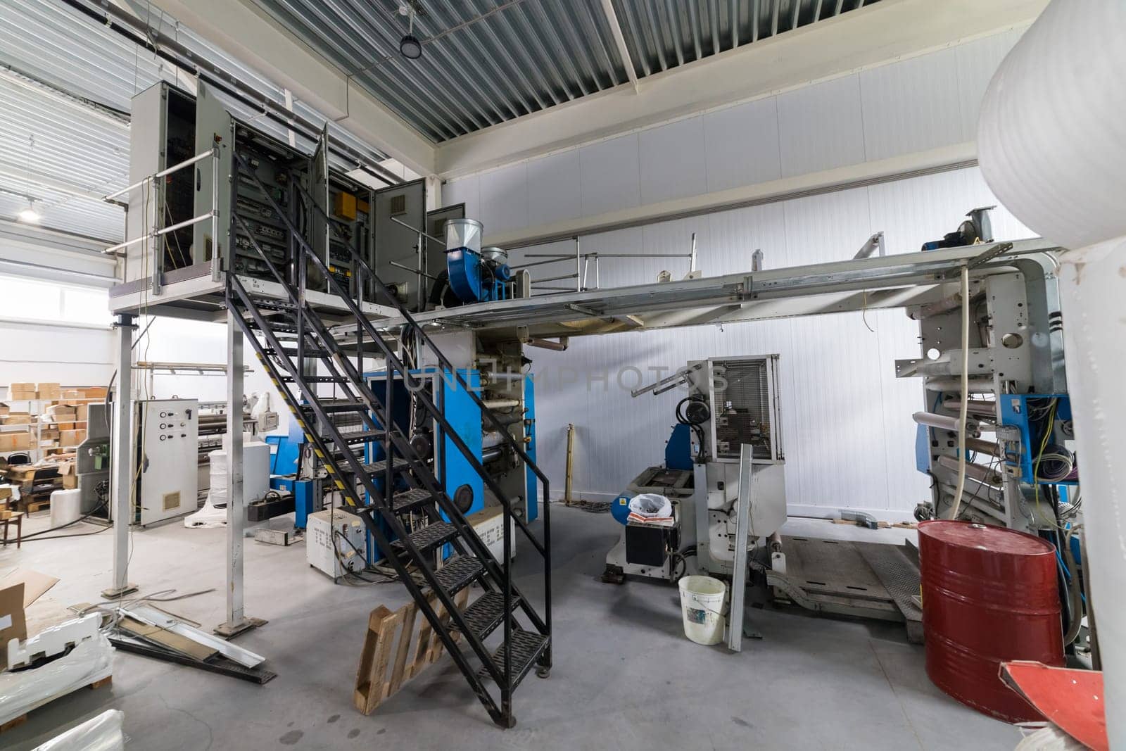 Large industrial printing press standing on a factory floor, surrounded by various equipment and materials, showcasing the scale of modern manufacturing